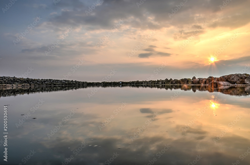 A colorful sunset sky reflects in the perfectly still waters of a rock-lined pool on the beach in Morecambe, Lancashire, England A colorful sunset sky reflects in the perfectly still waters of a rock-lined pool on the beach in Morecambe, Lancashire, England