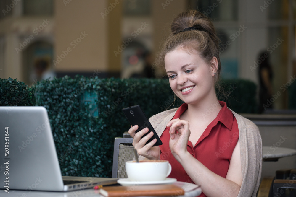 Young caucasian woman sitting in cafe and using her smartphone, smiling. Young caucasian woman sitting in cafe and using her smartphone, smiling.