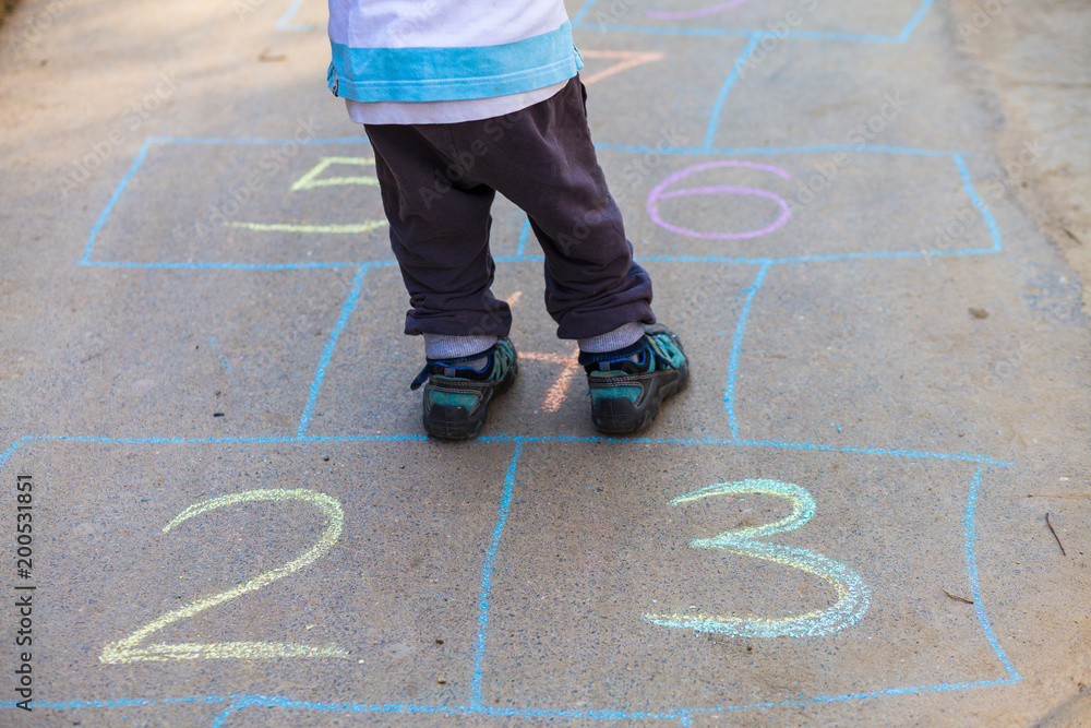 Hopscotch in a schoolyard on an asphalt floor with chalk drawings of numbers and squares as an