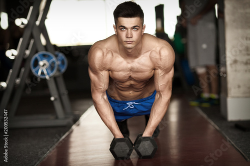 Strong, handsome man doing push-ups on dumbbells in a gym as bodybuilding exercise, training his muscles