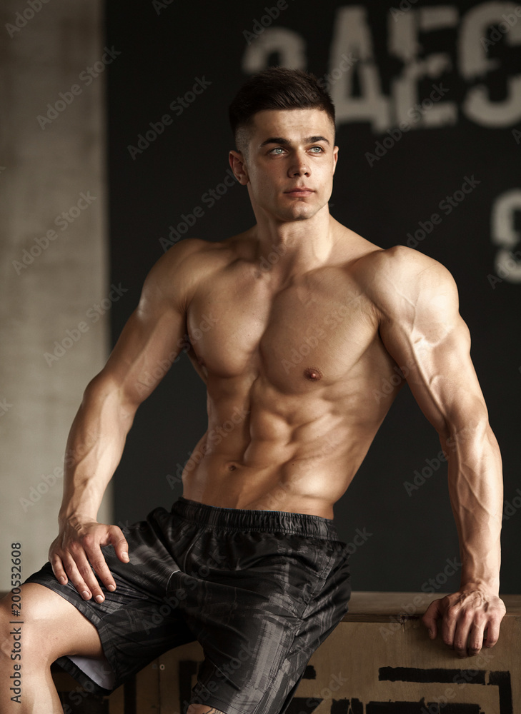 Fototapeta premium Healthy young man standing strong in the gym and flexing muscles - muscular athletic bodybuilder fitness model posing after exercises