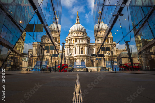 London, England - Beautiful St.Paul's Cathedral reflected in glass windows in the morning sunlight with iconic red double-decker bus and blue sky