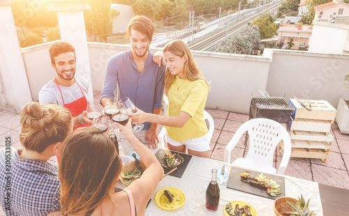 Young friends cheering with red wine at rooftop barbecue party photo