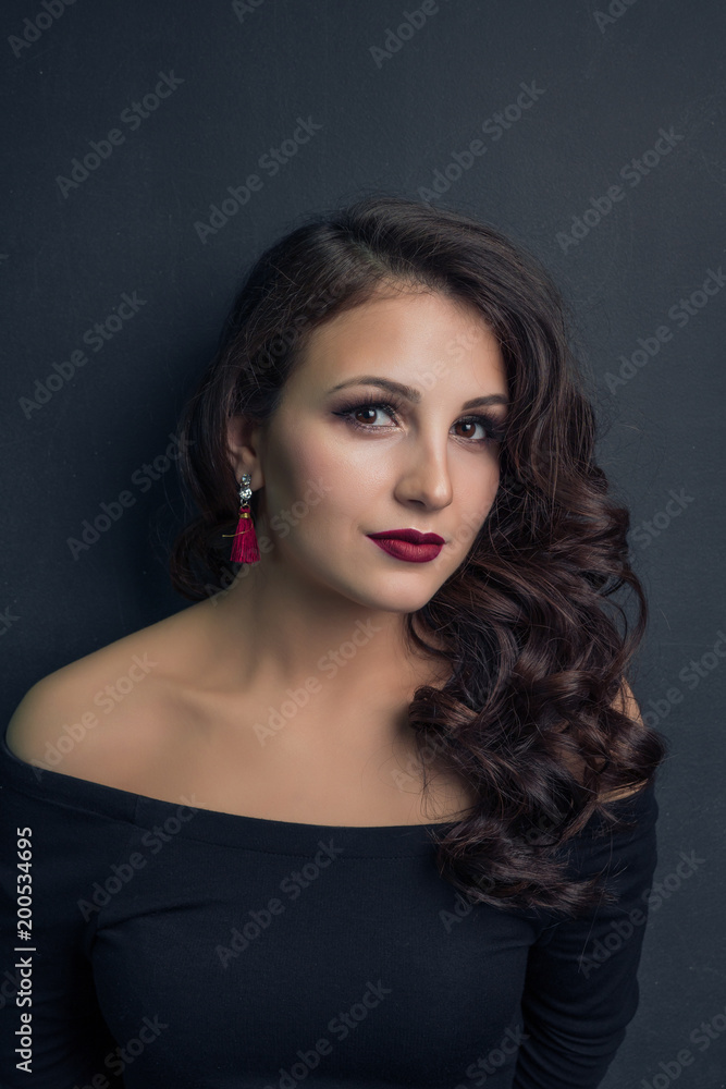Portrait of a brunette girl in a black dress on a dark background with bright earrings Portrait of a brunette girl in a black dress on a dark background with bright earrings