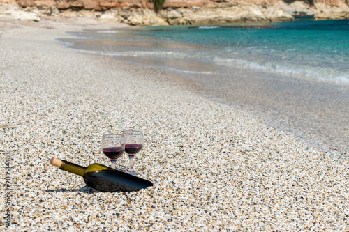 Glasses of red wine and bottle on the beach at the summer sunny day. Sea on the background.