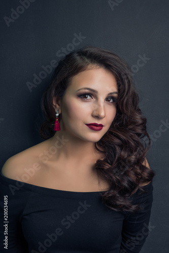 Portrait of a brunette girl in a black dress on a dark background with bright earrings