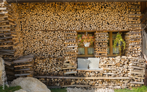 Summer cottage in village in Alps with big pile wood, grey stone, two windows and handmade seats for relax © Qe_Mogilev