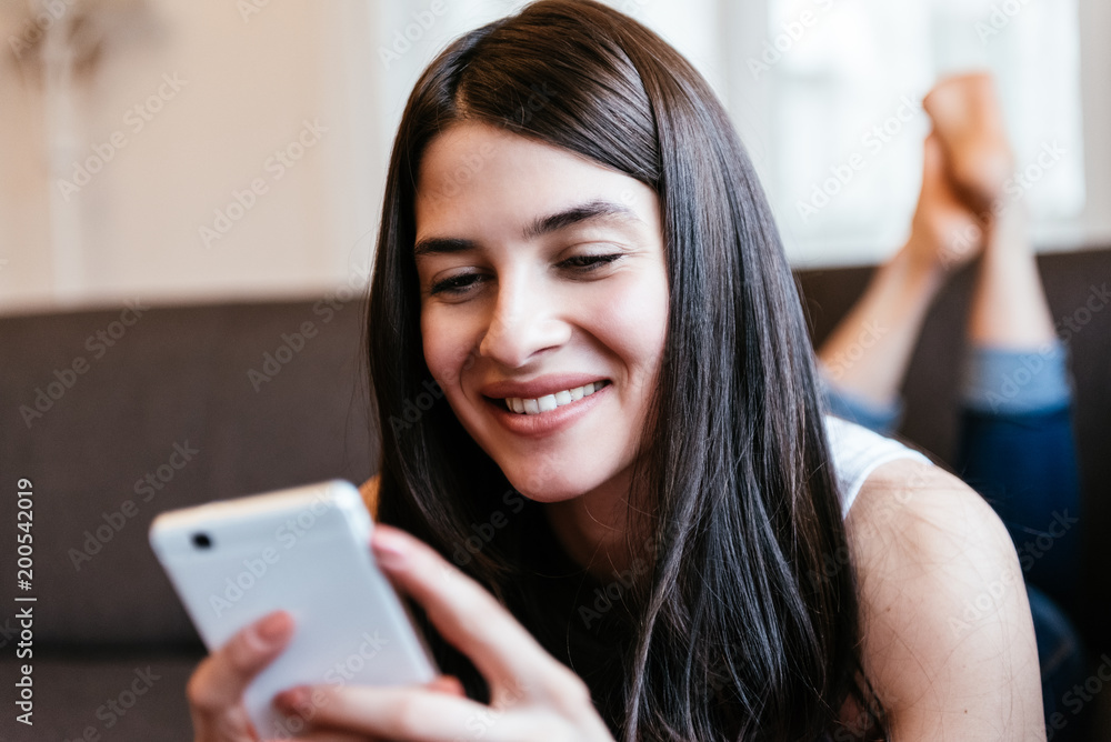Young beautiful woman relaxing on a sofa checking her emails and sms. Life style Young beautiful woman relaxing on a sofa checking her emails and sms. Life style