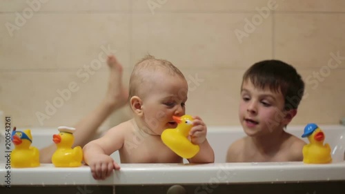 Little baby boy, playing with rubber ducks in bathtube with his siblings