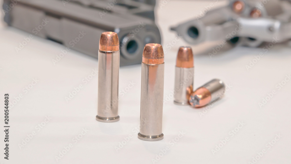 Four bullets, two 9mm and two .357 magnum with a stainless .357 revolver and a black 9mm pistol in the background Four bullets, two 9mm and two .357 magnum with a stainless .357 revolver and a black 9mm pistol in the background