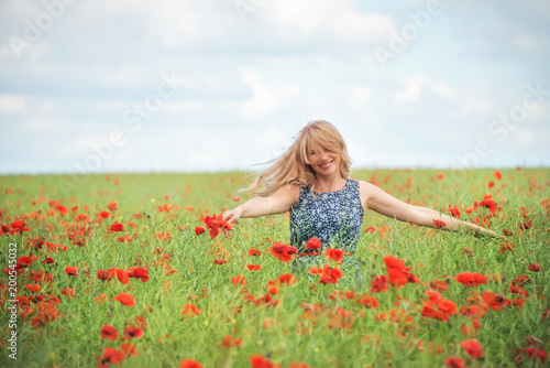 a natural woman with blond hair whirls in a field with beautiful red poppies. An atmosphere of carefree joy of happiness.
