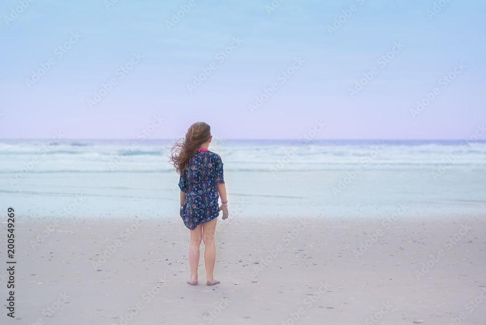 Young girl with long brown hair standing on the beach