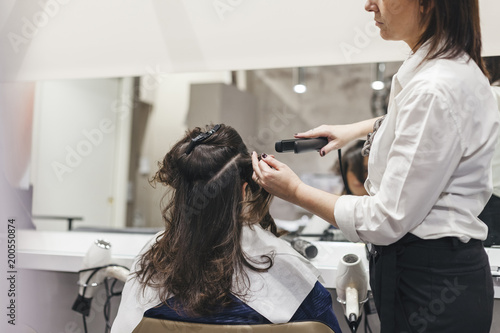 Hairdresser woman uses the straightener for styling of his young client in the salon