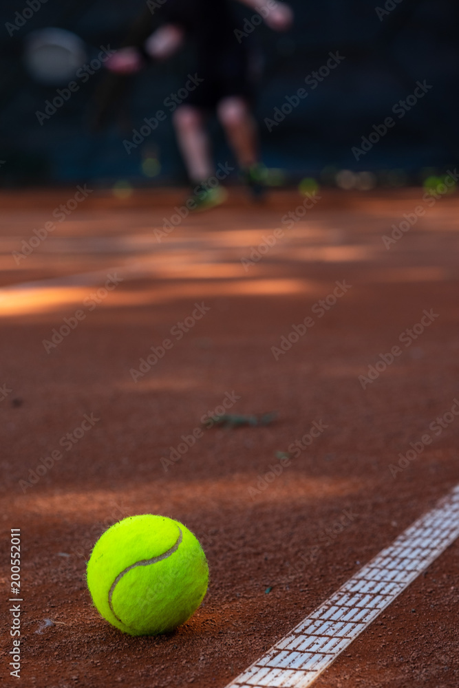 Closeup of tennis ball on a field with a blurred person playing in the background