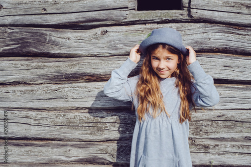 Joyful teen girl in casual clothes and blue hat posing by a wooden wall. Active lifestyle. Youth fashion