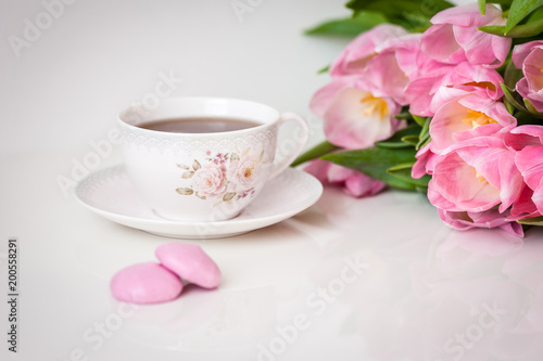 Bouquet of tulips and cup of tea on white background. Holiday card. Soft focus, copy space. Spring concept.