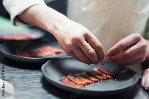 Restaurant Chef cook preparing tuna striped filet and crambling salad on the fish.
