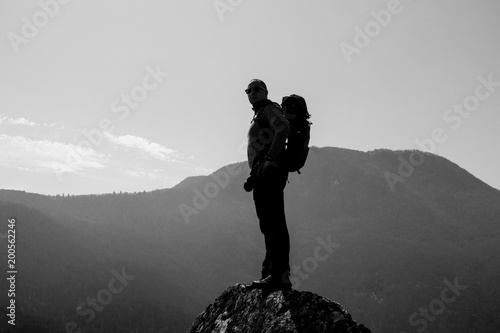 Successful young hiker standing on the top of the mountain and looking around.