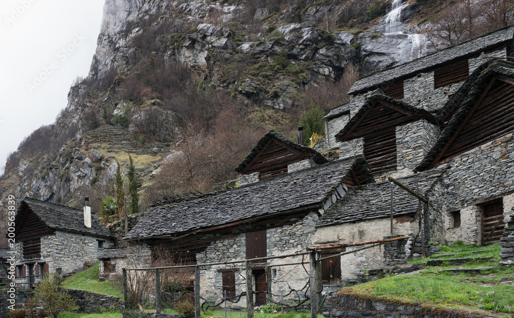 traditional alpine village with many small wooden and stone houses and a mountain waterfall backdrop