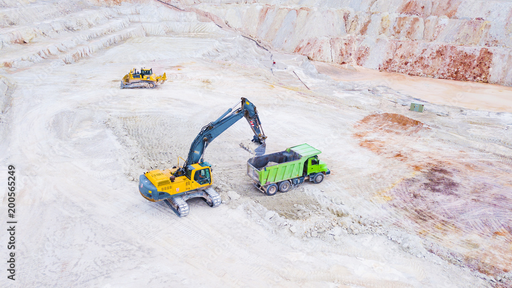 Aerial view of excavator loading dump truck with raw kaolin in kaolin quarry for ceramic tiles production. Industrial area from above. Kaznejov, Czech republic, European union.