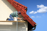 Mężczyzna, malarz maluje farbą okap czerwoego dachu.