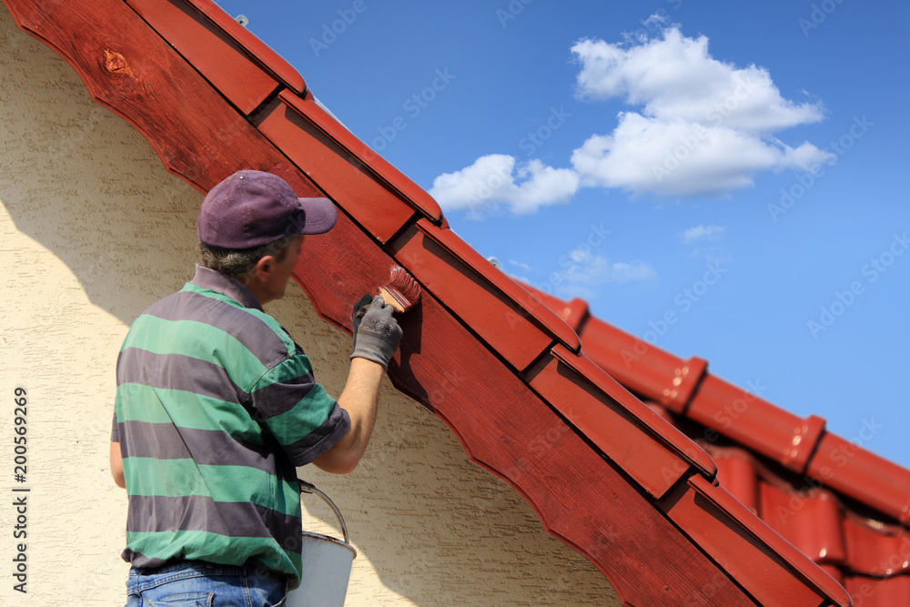 Mężczyzna, malarz maluje farbą okap czerwoego dachu. - obrazy, fototapety, plakaty 