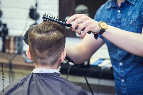 Hairdresser making a hairstyle to a boy in London barbershop.