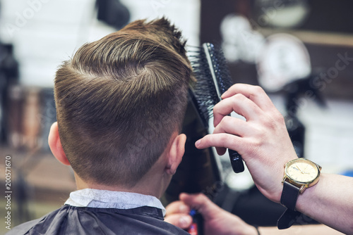 Boy getting hairstyle by hairdresser in barbershop.