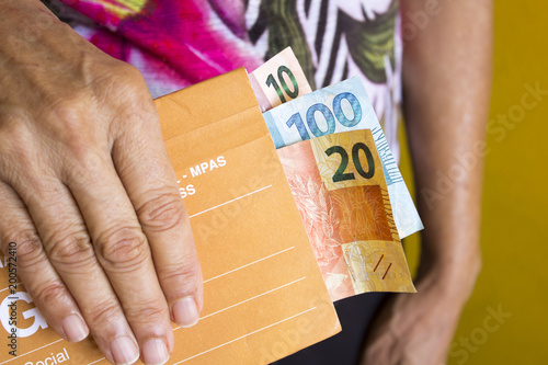 Idosa segurando boleto com dinheiro brasileiro para previdência social aposentadoria photo