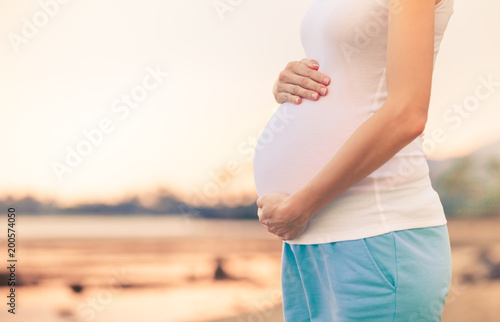 Closeup of pregnant woman belly against beautiful sunset. 