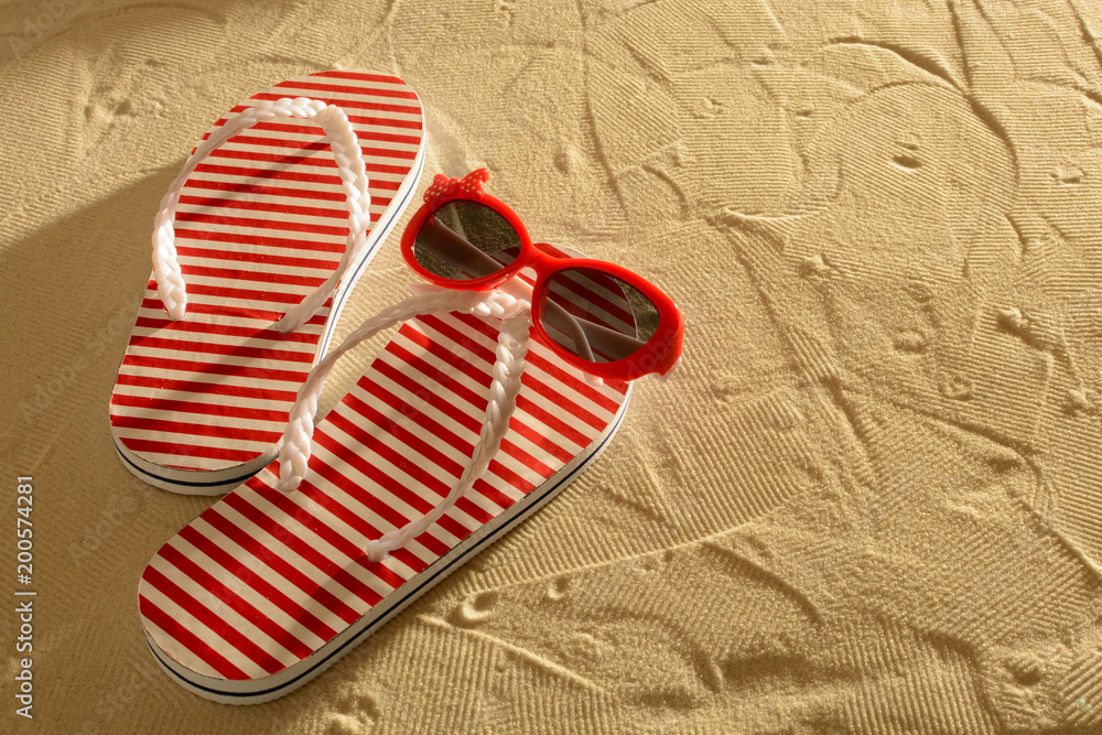 Naklejka premium Sandal and sunglasses on a sandy beach, sunset, top view