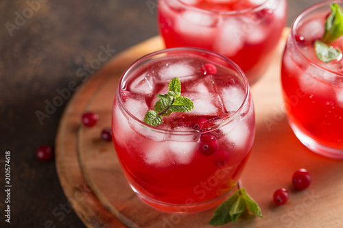 Summer cranberry drink with mint and ice cubes in three glasses on wooden cutting board.