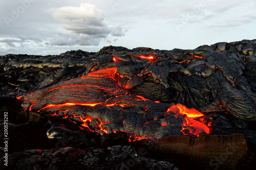 A lava flow emerges from an earth column and flows in a black volcanic landscape, in the sky shows the first daylight - Location: Hawaii, Big Island, volcano 