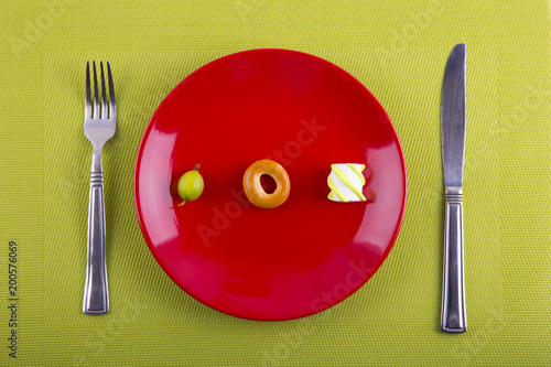 Minimalistic food composition with different types of products on red plate, knife and fork on green background