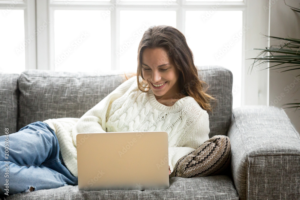 Smiling young woman enjoying using laptop relaxing at home on sofa, beautiful happy mestizo girl typing on computer having fun online doing internet shopping or chatting with friends lying on couch Smiling young woman enjoying using laptop relaxing at home on sofa, beautiful happy mestizo girl typing on computer having fun online doing internet shopping or chatting with friends lying on couch