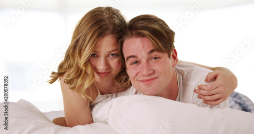 Young attractive couple lying in bed together laughing and looking at camera