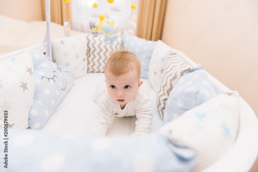 Cute baby lies on her stomach in a white round bed. Light nursery for young children. Cute baby lies on her stomach in a white round bed. Light nursery for young children.