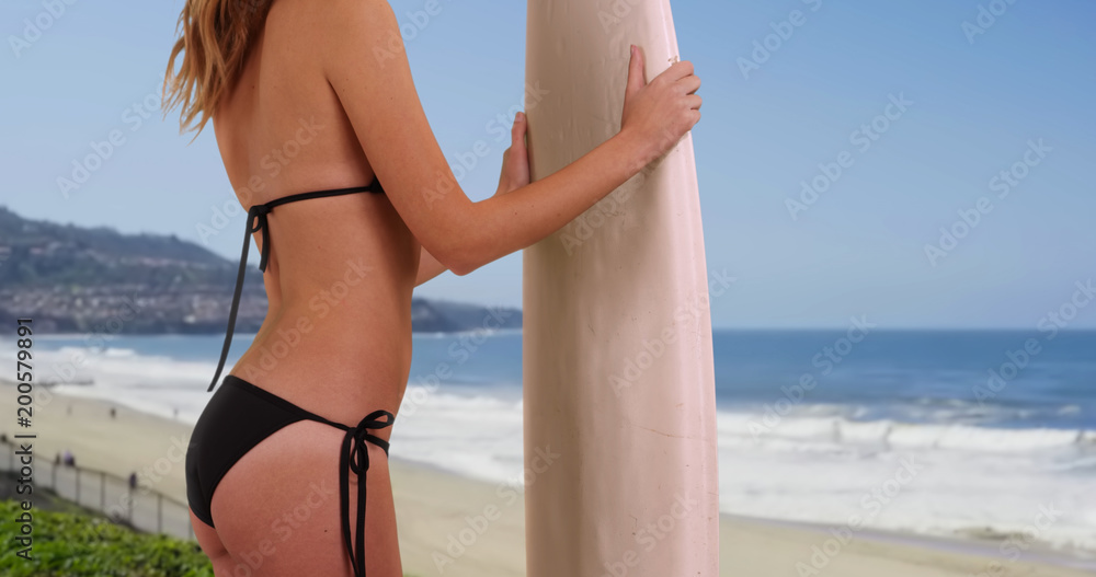 Profile of young Caucasian woman in string bikini holding surfboard on the  coast Stock Photo | Adobe Stock