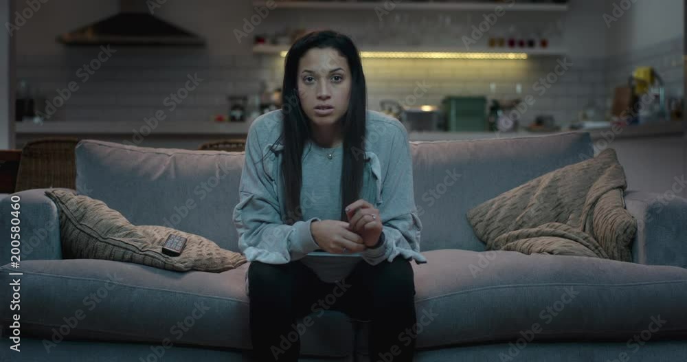 An woman sits on the edge of a sofa, captivated by something she is watching on tv. An woman sits on the edge of a sofa, captivated by something she is watching on tv.