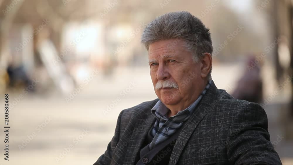 Profile of a wise senior man with a white mustache sitting on a bench and enjoying his life in an alley on a sunny day in spring Profile of a wise senior man with a white mustache sitting on a bench and enjoying his life in an alley on a sunny day in spring