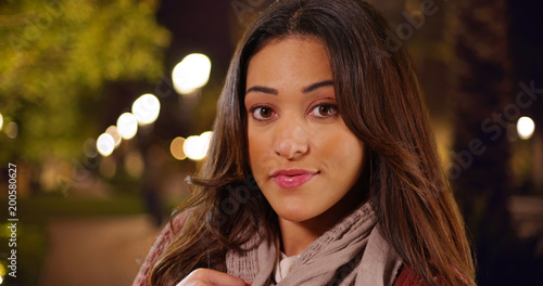 Closeup of cheerful Hispanic female standing in park at night smiling at camera 