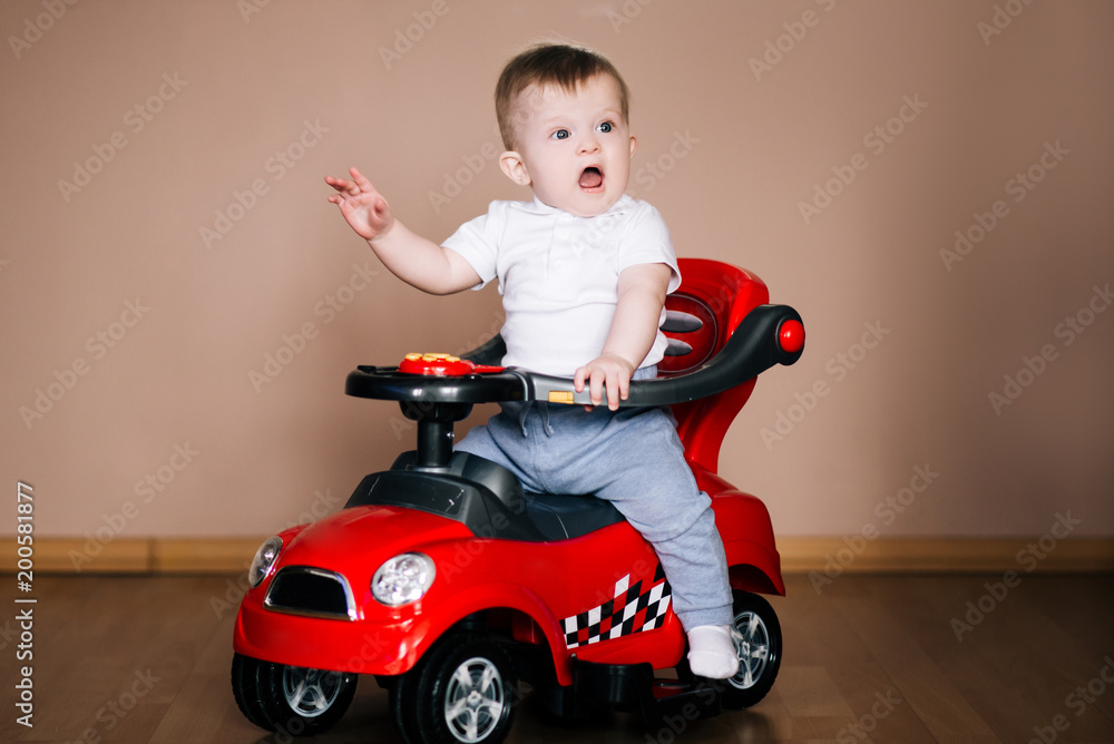 Cute young emotional baby sitting in a toy red car, screaming, playing Cute young emotional baby sitting in a toy red car, screaming, playing