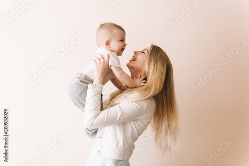 You are my treasure! cheerful beautiful young woman holding baby boy in her hands and looking at him with love  at home