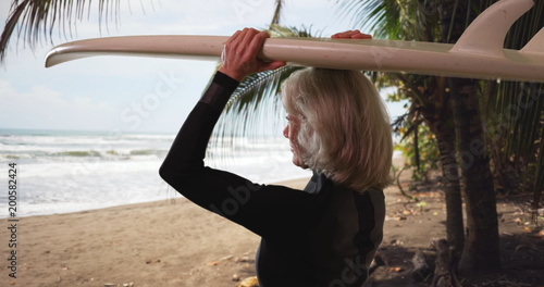 Canvas Print Active elderly female surfer with surfboard in tropical beach setting enjoying v