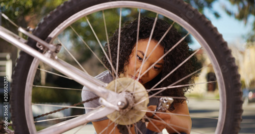Smart black millennial woman fixing bicycle outside in suburban neighborhood
