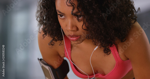 Fotografie Strong African-American fitness girl with earphones in breathing heavily indoors