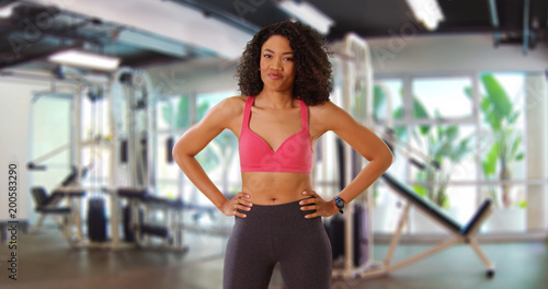 Spunky black woman athlete standing with hands at hips by workout equipment