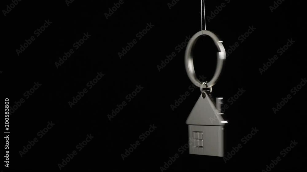 Metal key holder with house shape hanging and rotating on black background Metal key holder with house shape hanging and rotating on black background