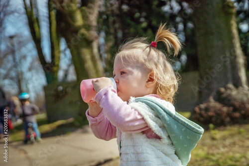 Little baby girl on a walk in the Park drinking from a bottle.
