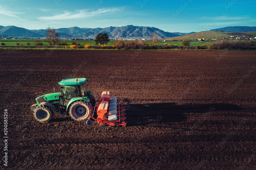 Naklejka premium Farmer with tractor seeding crops at field